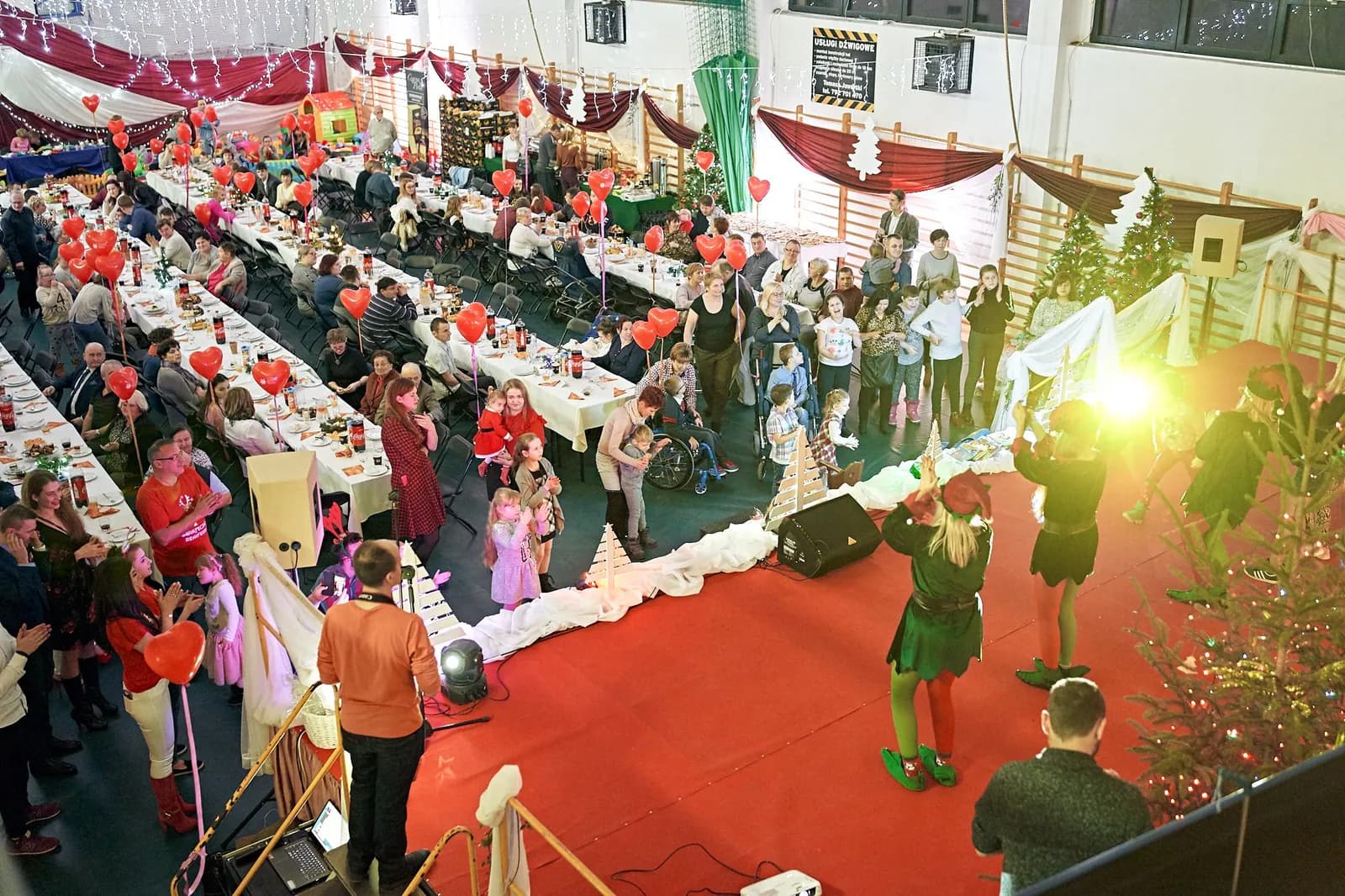 Mikołajki dla kilkuset osób w hali — scena, choinki i czerwony dywan