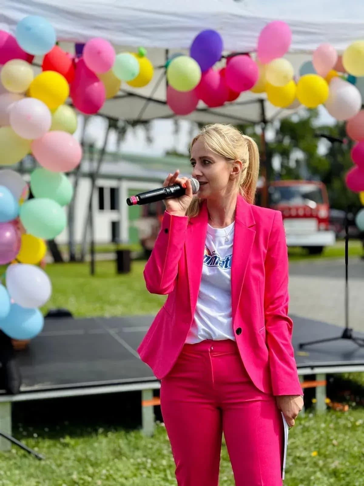 Prowadząca z mikrofonem na scenie plenerowej wśród balonów