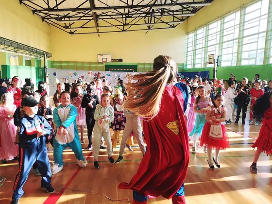 Bal w sali gimnastycznej — dzieci w strojach karnawałowych w kręgu