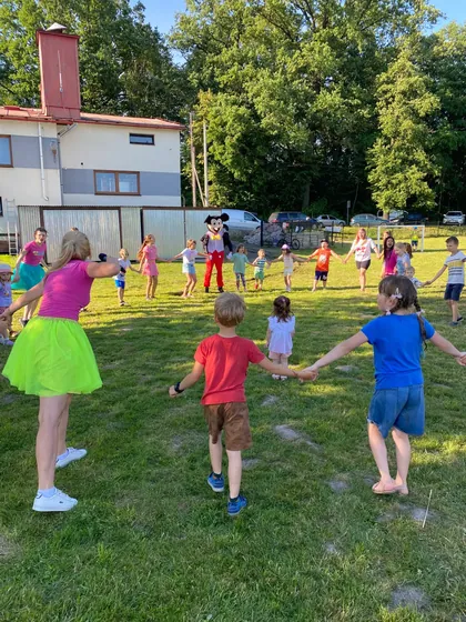 Dzieci trzymają się za ręce w kole na trawie podczas gier plenerowych