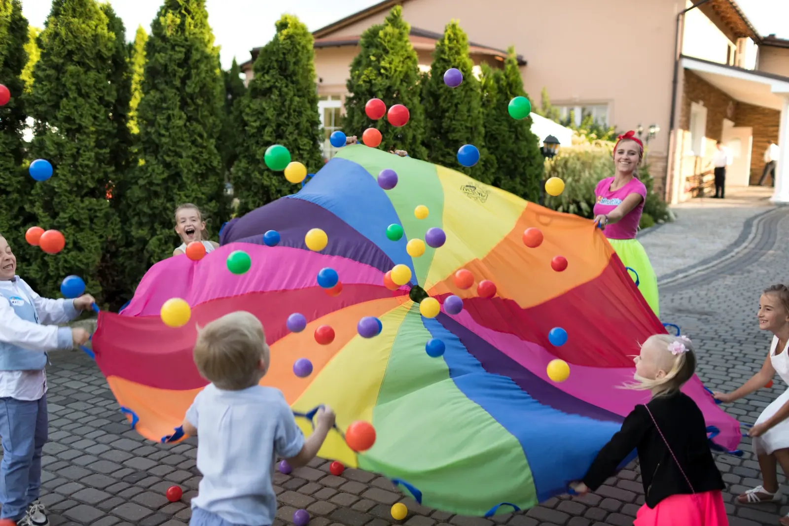 Tęczowa chusta animacyjna z piłeczkami podczas zabawy przed budynkiem